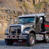 Gray Mack dump truck parked in rocky quarry with stone cliff background