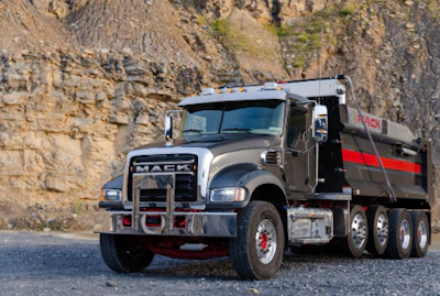 Gray Mack dump truck parked in rocky quarry with stone cliff background