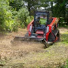 Red Manitou tracked skid steer mulching forest floor with brush attachment