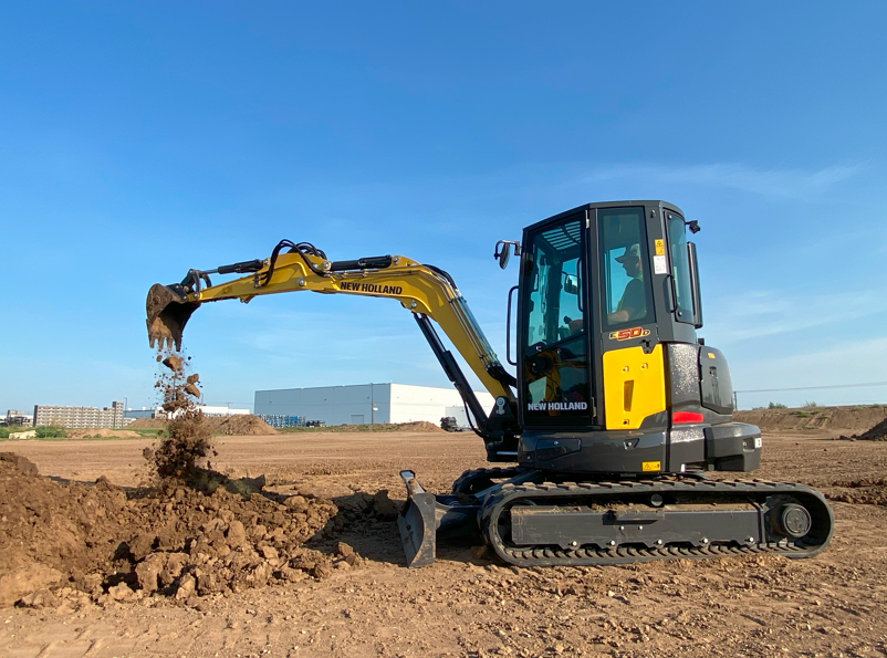 Yellow New Holland excavator digging dirt on construction site with blue sky
