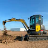 Yellow New Holland excavator digging dirt on construction site with blue sky