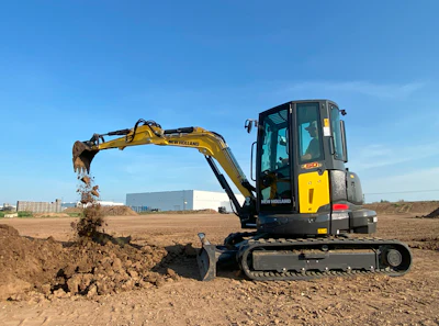 Yellow New Holland excavator digging dirt on construction site with blue sky
