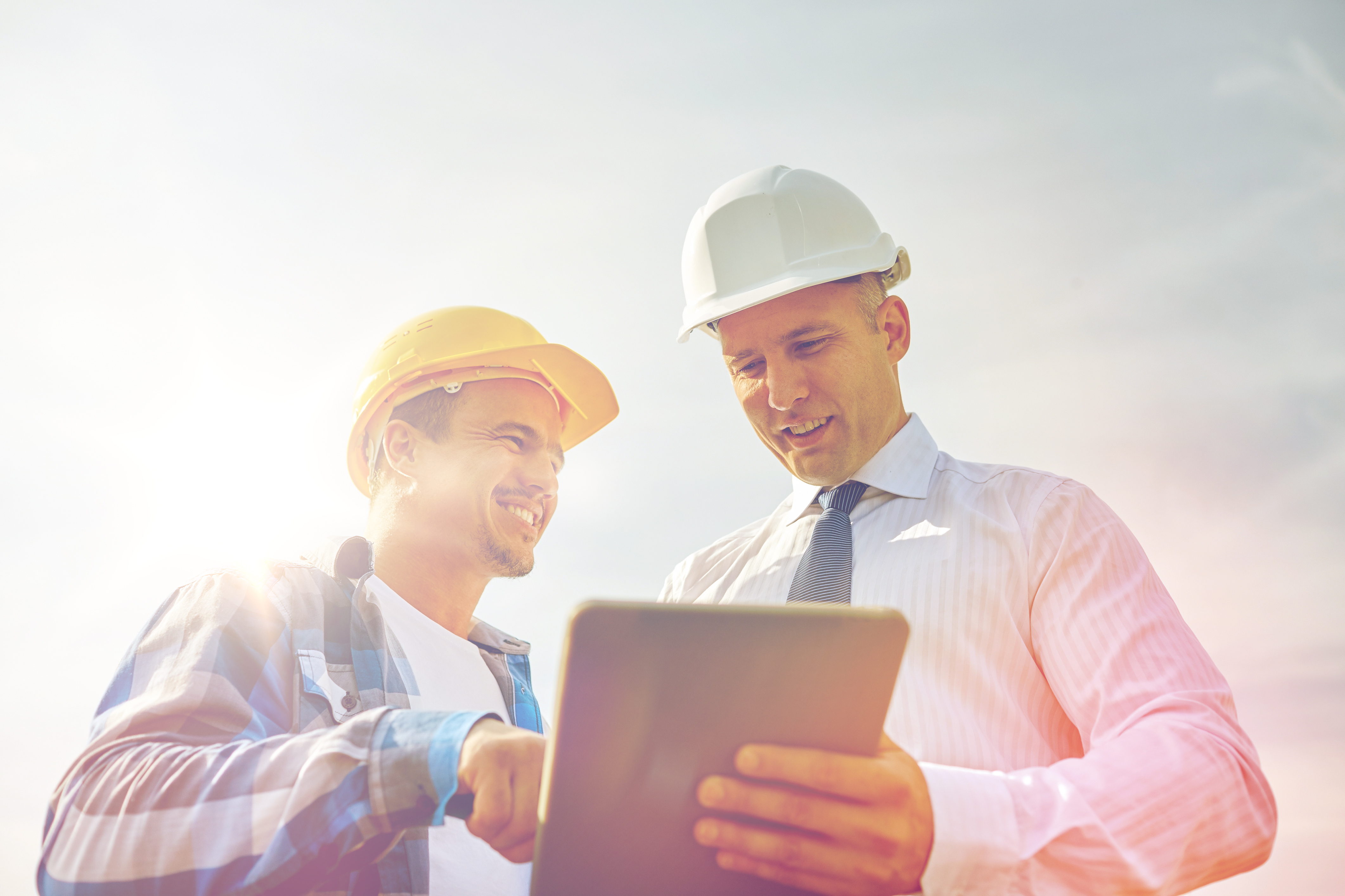 Construction workers in hard hats reviewing project details on a tablet outdoors