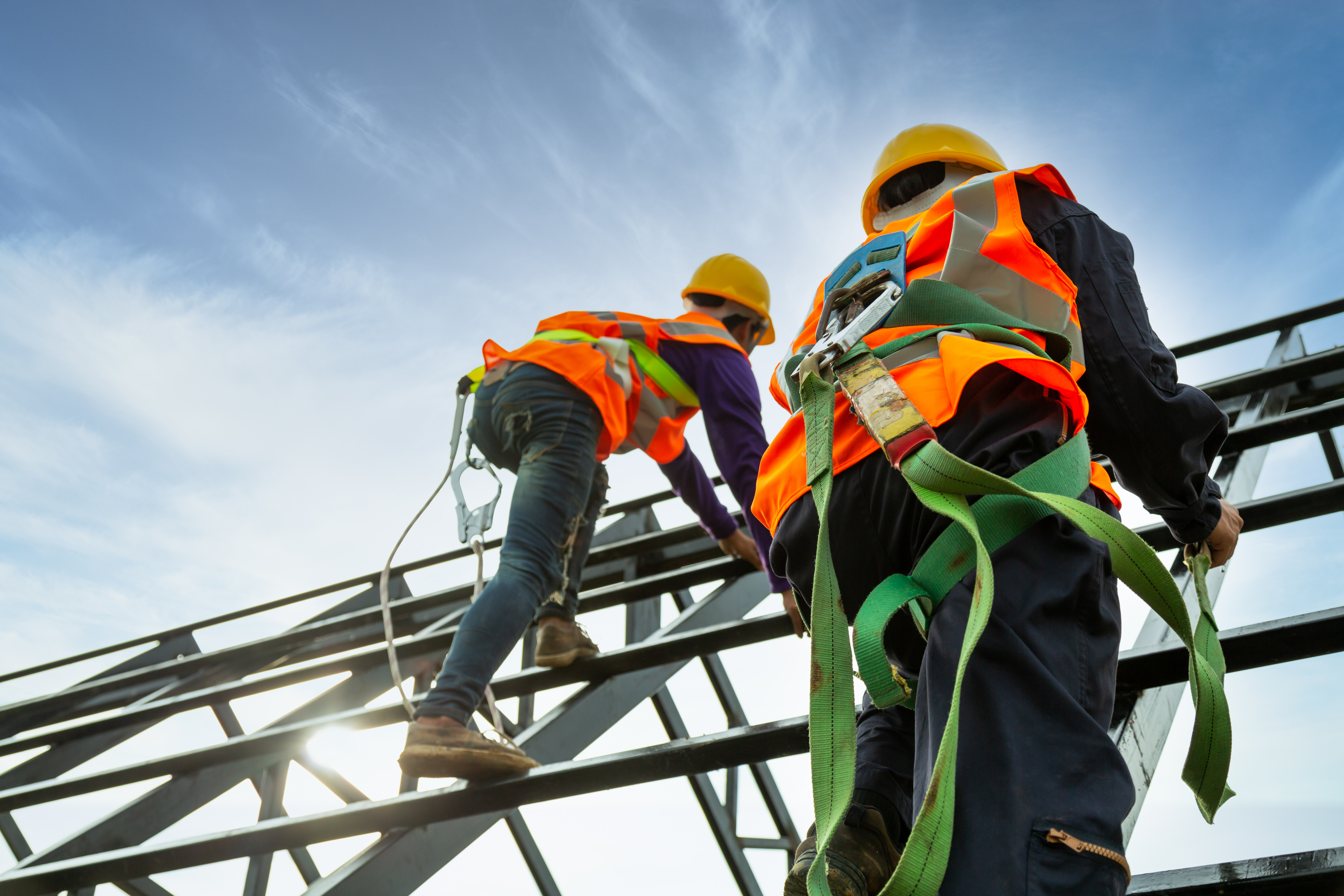 Construction workers in safety gear climbing metal scaffolding against blue sky