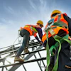 Construction workers in safety gear climbing metal scaffolding against blue sky
