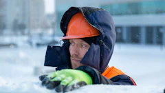 Construction worker in orange hard hat and winter gear standing in snowy outdoor setting