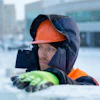 Construction worker in orange hard hat and winter gear standing in snowy outdoor setting