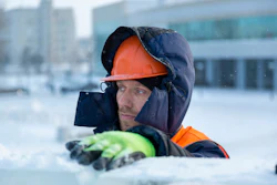 Construction worker in orange hard hat and winter gear standing in snowy outdoor setting