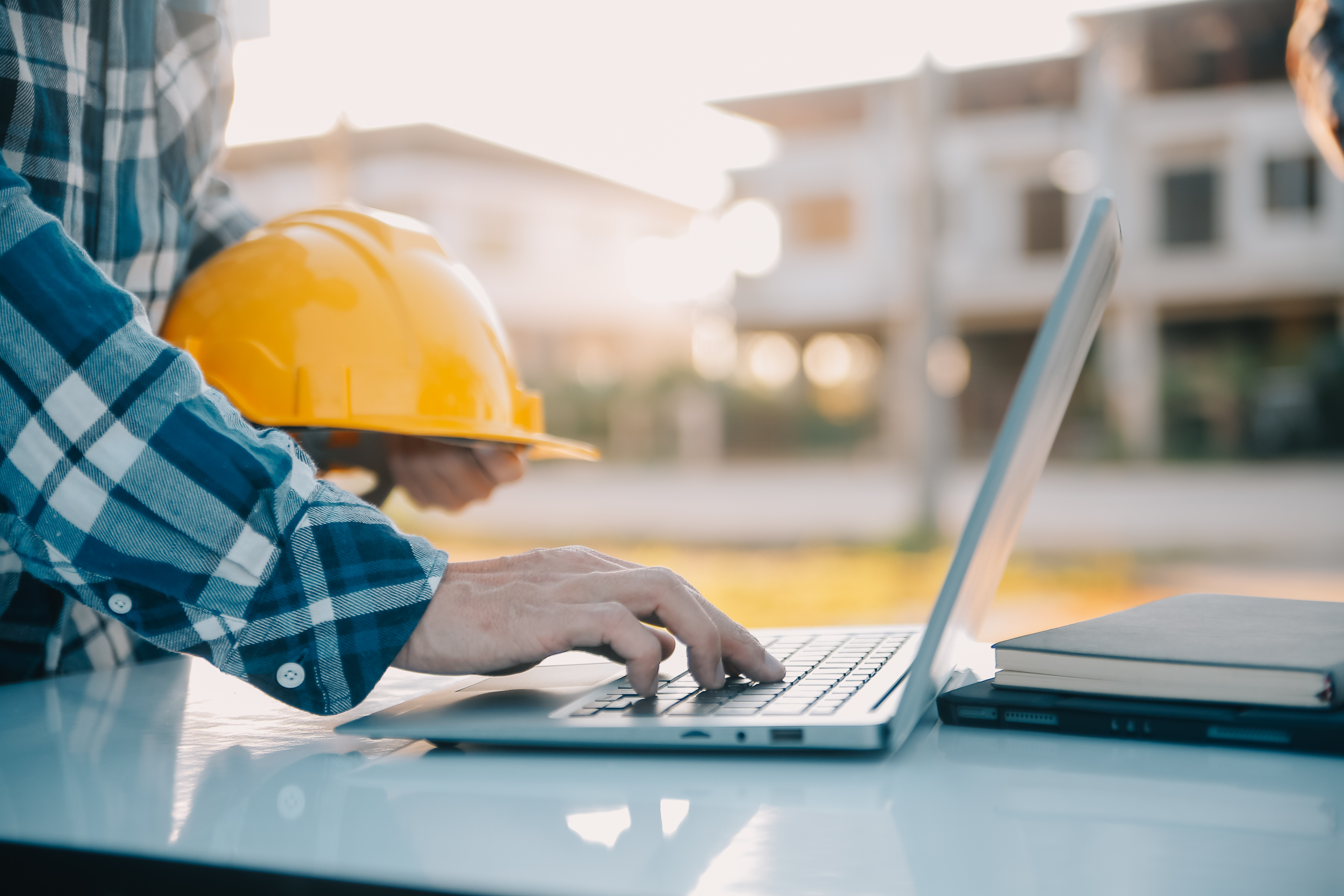 Construction worker using laptop at worksite with yellow hard hat