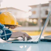 Construction worker using laptop at worksite with yellow hard hat