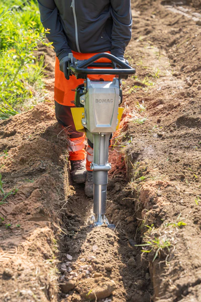 Construction worker operating a Bomag jackhammer to dig a trench in soil