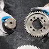 Industrial metal gears with blue-tipped work gloves on textured surface