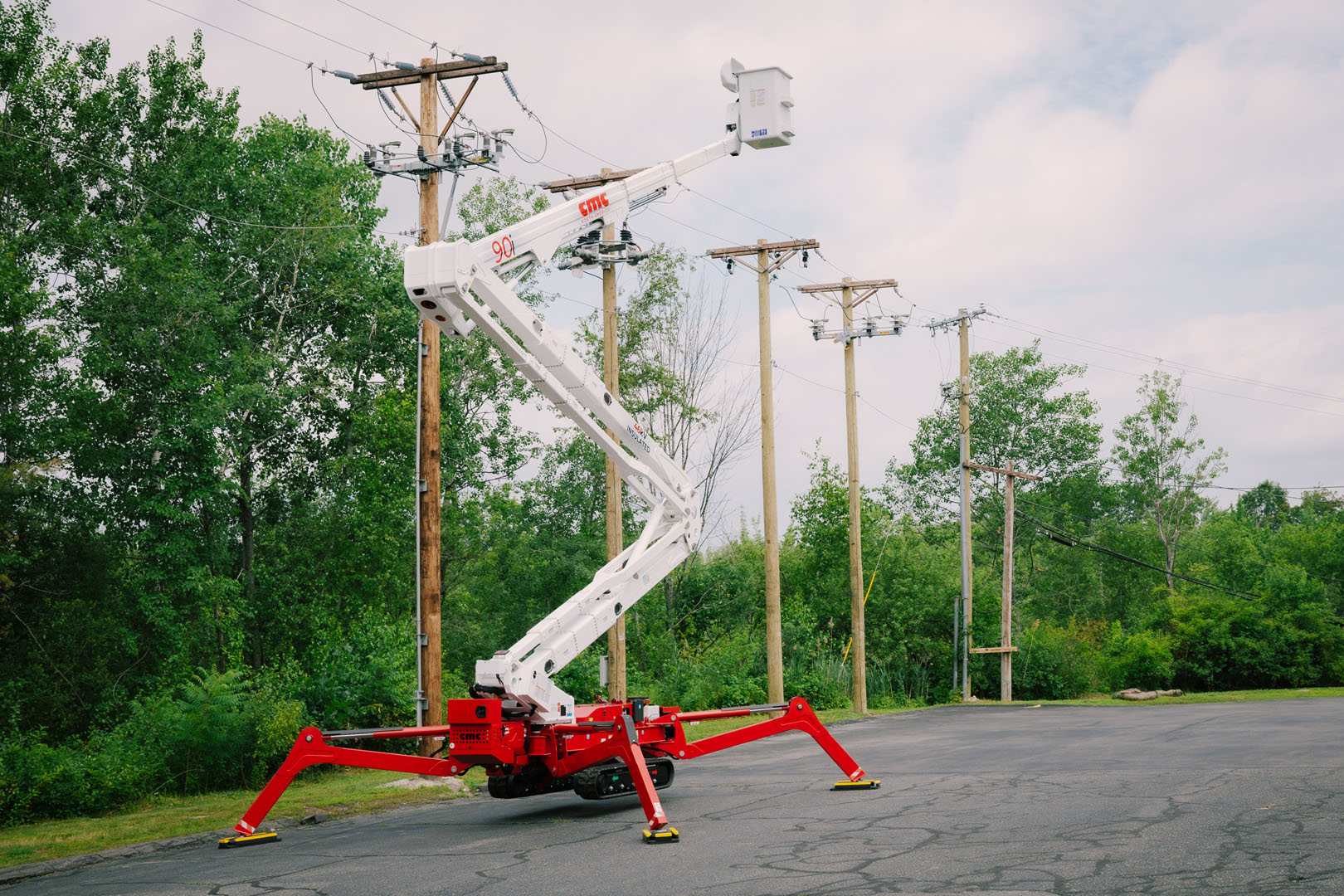 Red and white spider lift extended near utility poles in tree-lined parking area