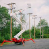 Red and white spider lift extended near utility poles in tree-lined parking area