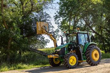 Green John Deere tractor parked on dirt road surrounded by trees