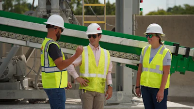 Three construction workers in safety vests and hard hats near industrial machinery