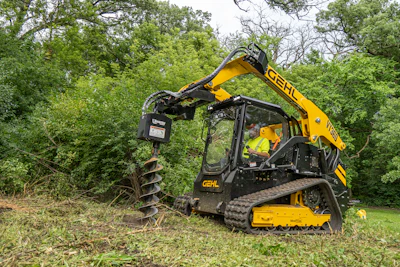 Yellow Gehl skid steer loader with auger attachment drilling into grassy terrain