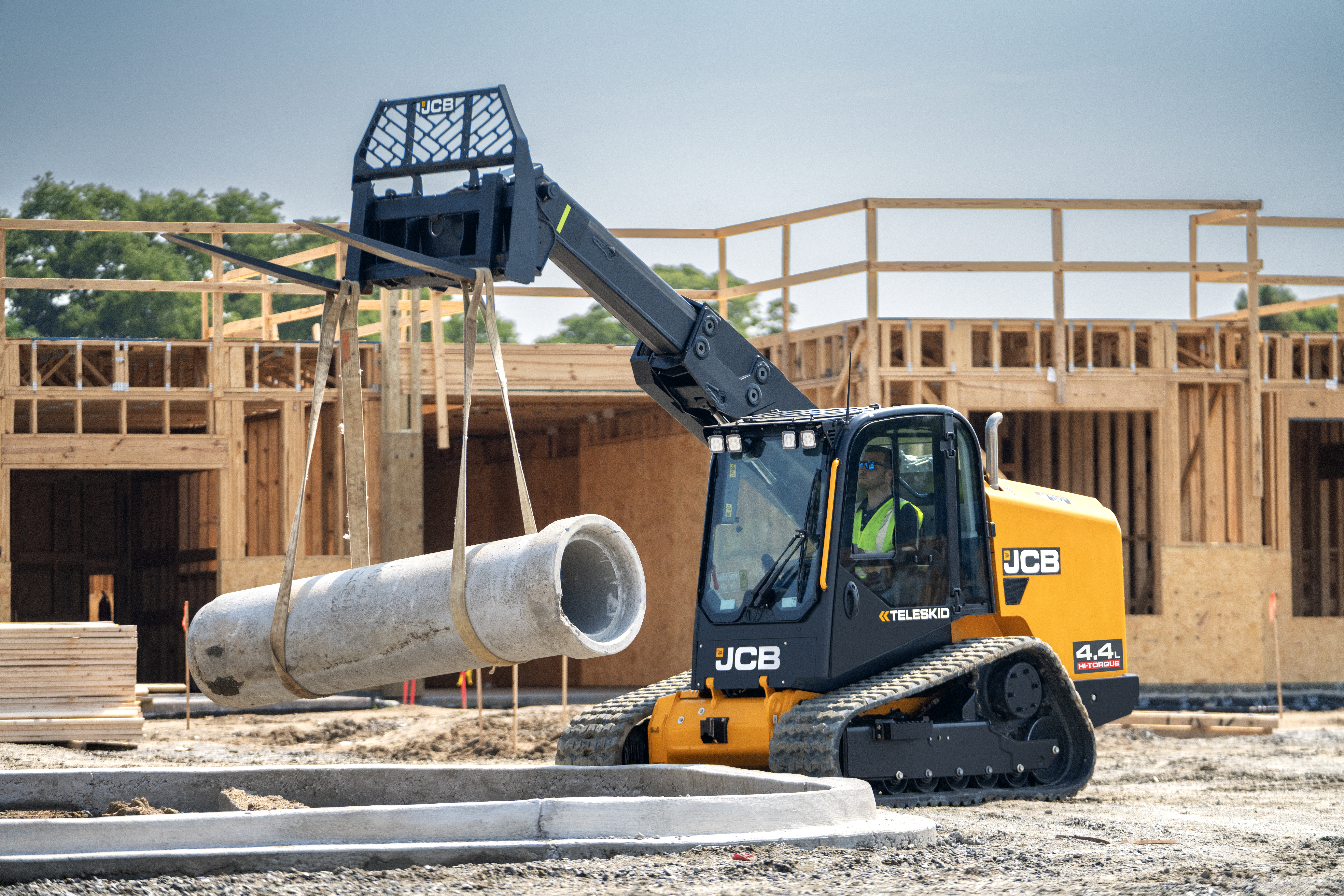Yellow JCB tracked loader lifting large concrete pipe at construction site