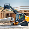 Yellow JCB tracked loader lifting large concrete pipe at construction site
