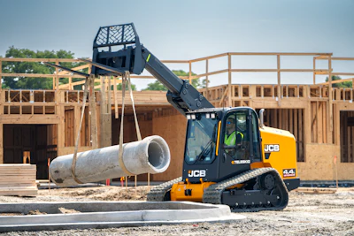 Yellow JCB tracked loader lifting large concrete pipe at construction site