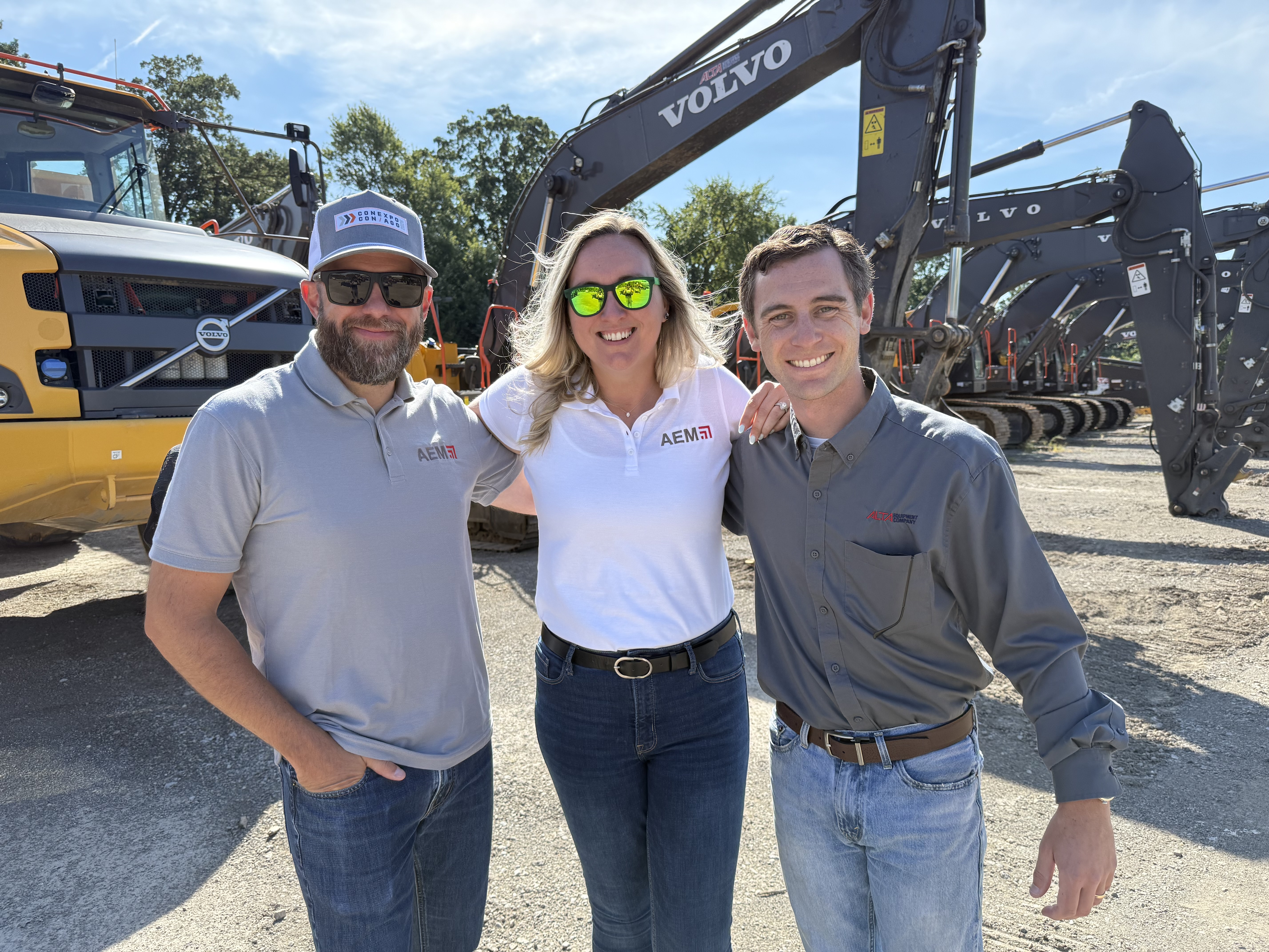 Three professionals standing near Volvo excavators at construction equipment site