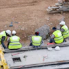 Construction workers in high-visibility vests examine site foundation work