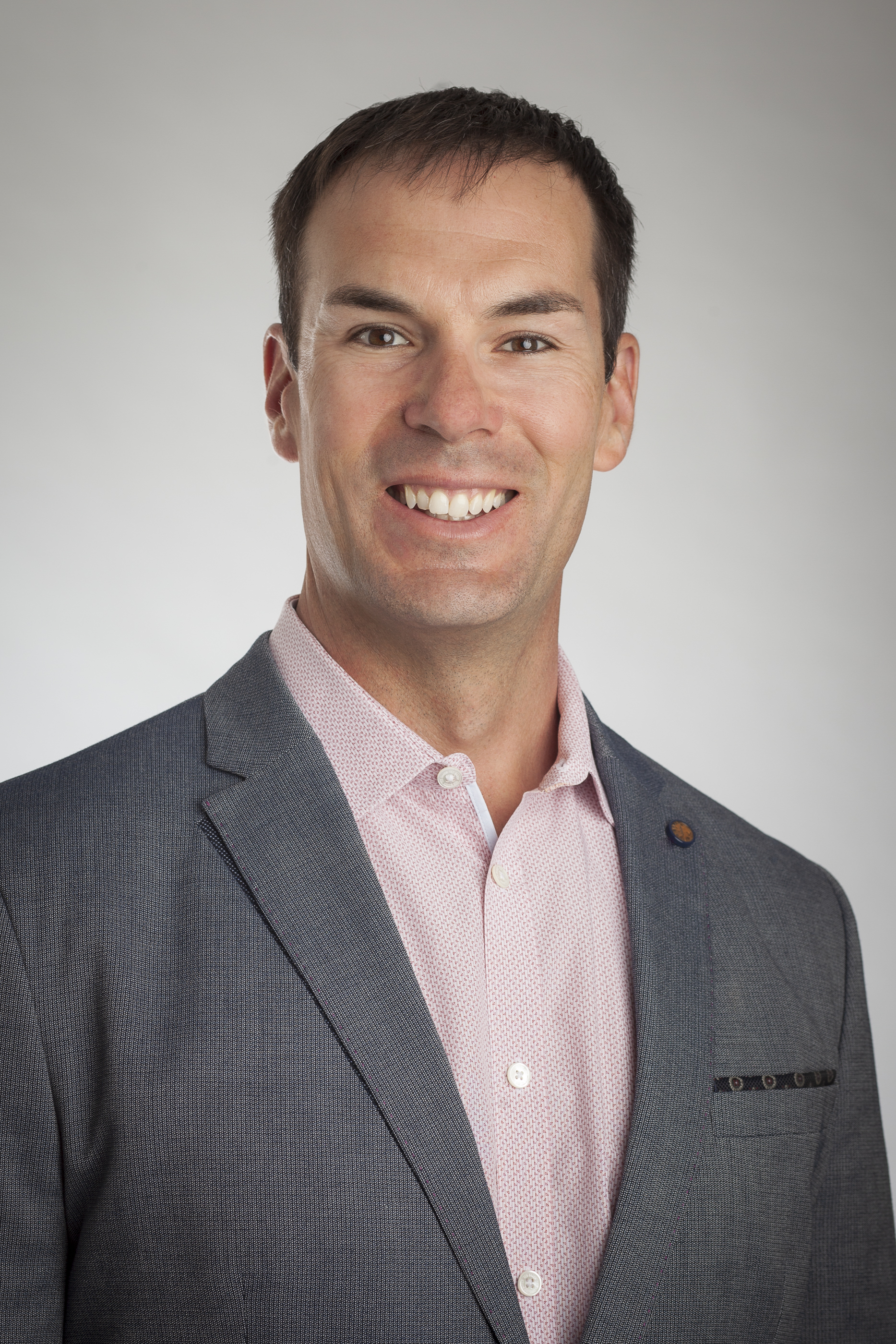 Smiling professional in gray suit and pink shirt against neutral background Headshot