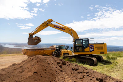 Yellow Komatsu excavator loading soil at construction site with dump truck