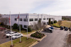 Corporate office building with flags, landscaped parking area and parked vehicles