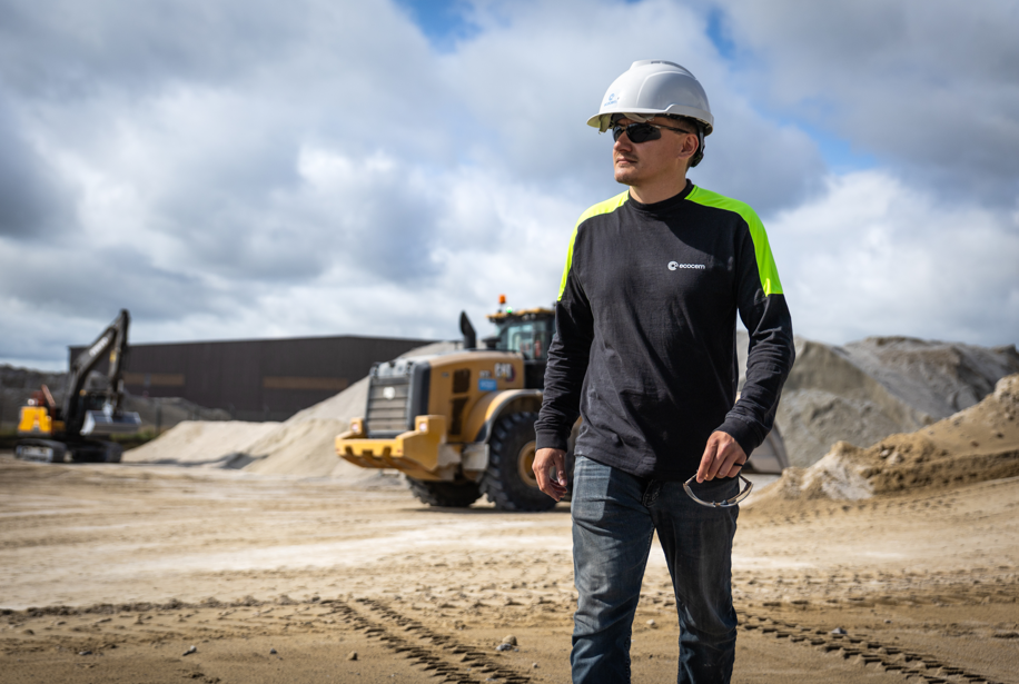 Construction worker in safety gear standing near heavy equipment on sandy worksite
