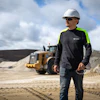 Construction worker in safety gear standing near heavy equipment on sandy worksite