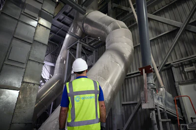 Industrial worker in safety vest inspecting large metal ventilation pipes in manufacturing facility