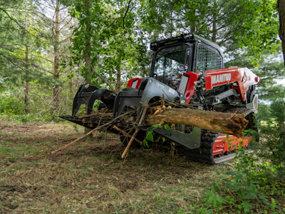 Red Manitou forestry machine moving fallen tree logs in wooded forest area