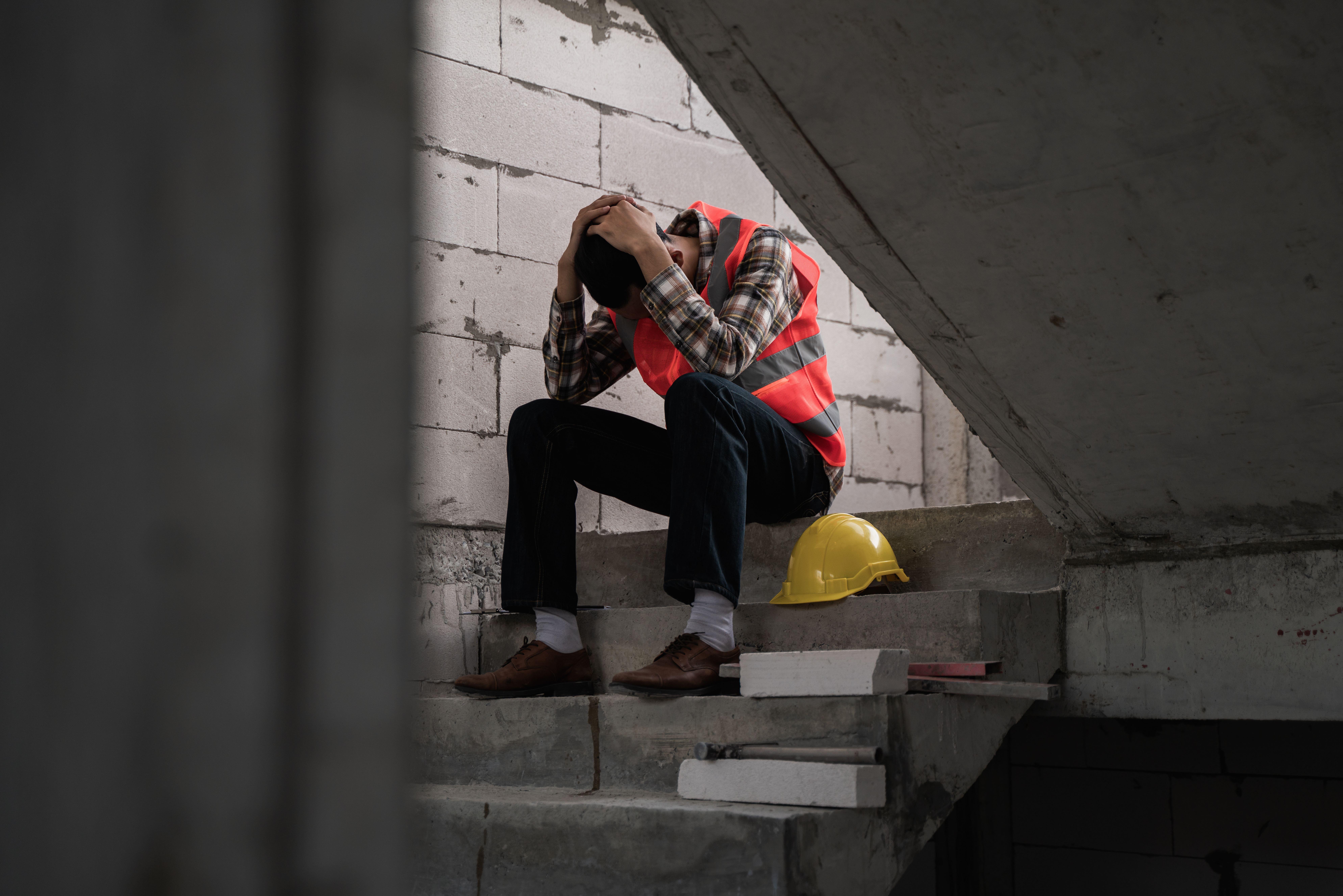 Construction worker sitting on stairs, head in hands, yellow hard hat nearby