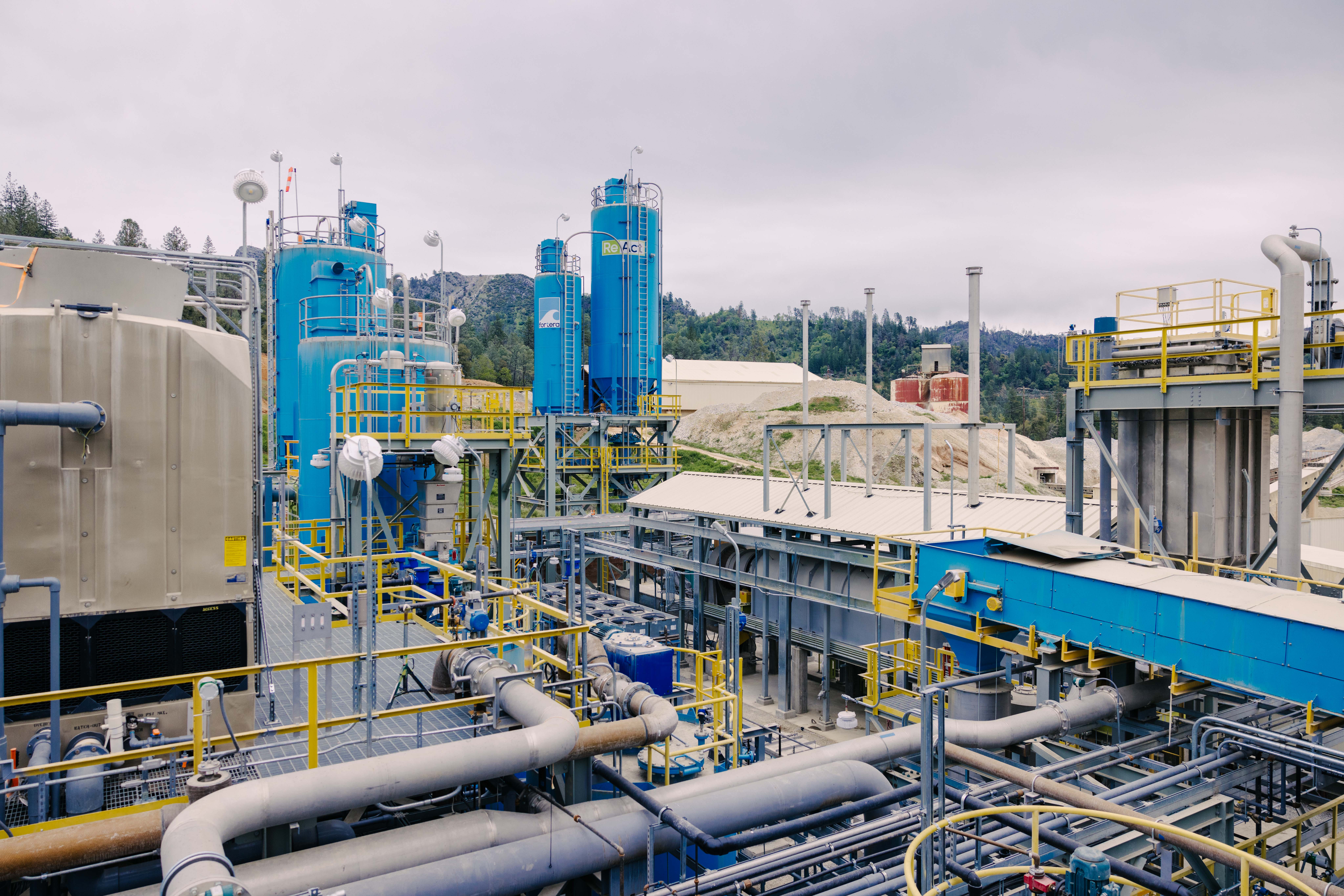 Industrial processing plant with blue and gray machinery, pipelines, and storage tanks