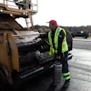 Construction worker operating asphalt paving machine on roadway