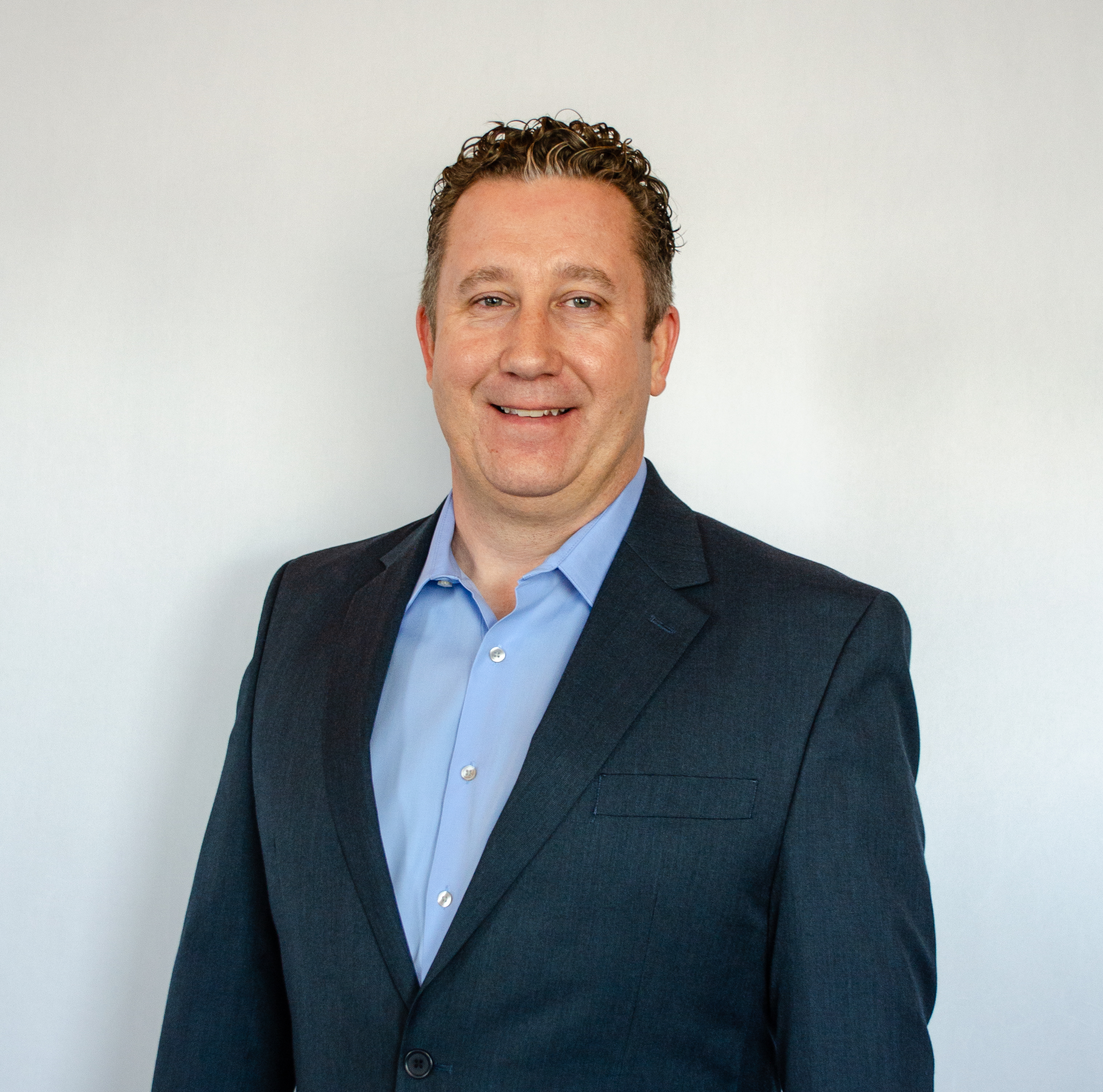 Smiling professional in navy blazer and blue shirt against neutral background Headshot