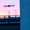Drone hovering near concrete wall with power transmission towers at twilight