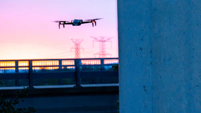 Drone hovering near concrete wall with power transmission towers at twilight
