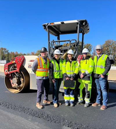 Construction team in high-visibility vests standing near road roller on fresh asphalt