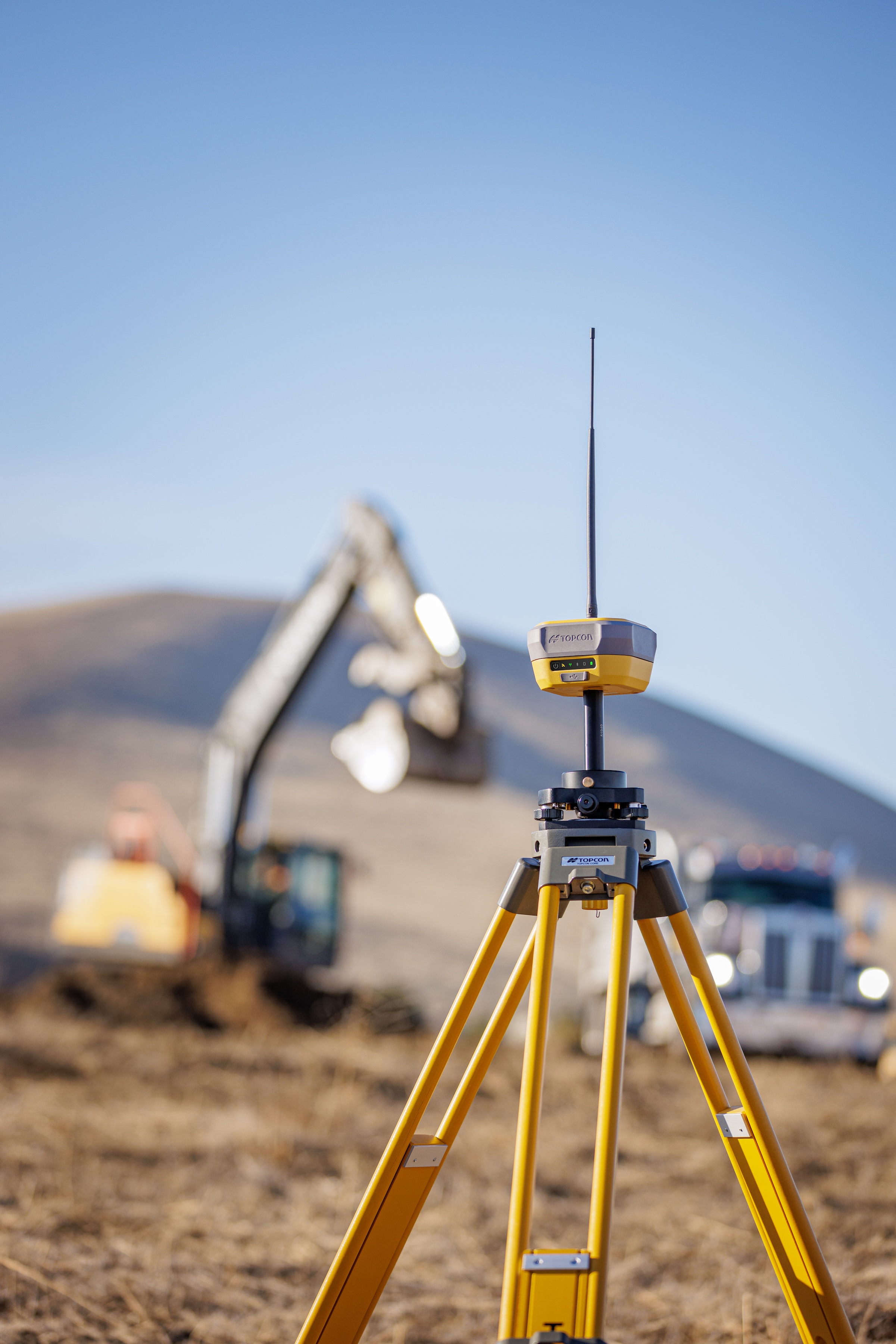 Yellow surveying GPS equipment on tripod at construction site with excavator in background
