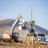 Yellow surveying GPS equipment on tripod at construction site with excavator in background