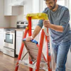 Person using a red ladder to work in a kitchen with stainless steel appliances