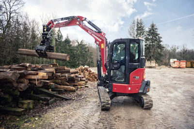 Red compact excavator moving timber logs at a forestry work site