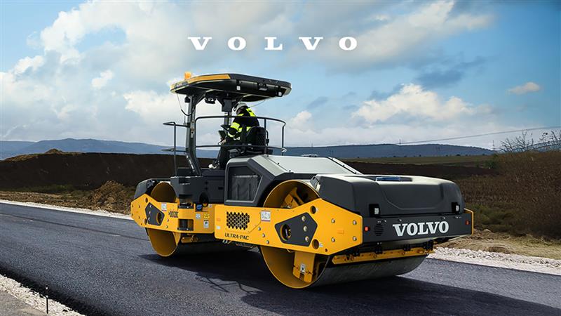 Volvo road roller compacting fresh asphalt on highway with mountain landscape