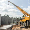Yellow mobile crane positioned near concrete wall panels at construction site