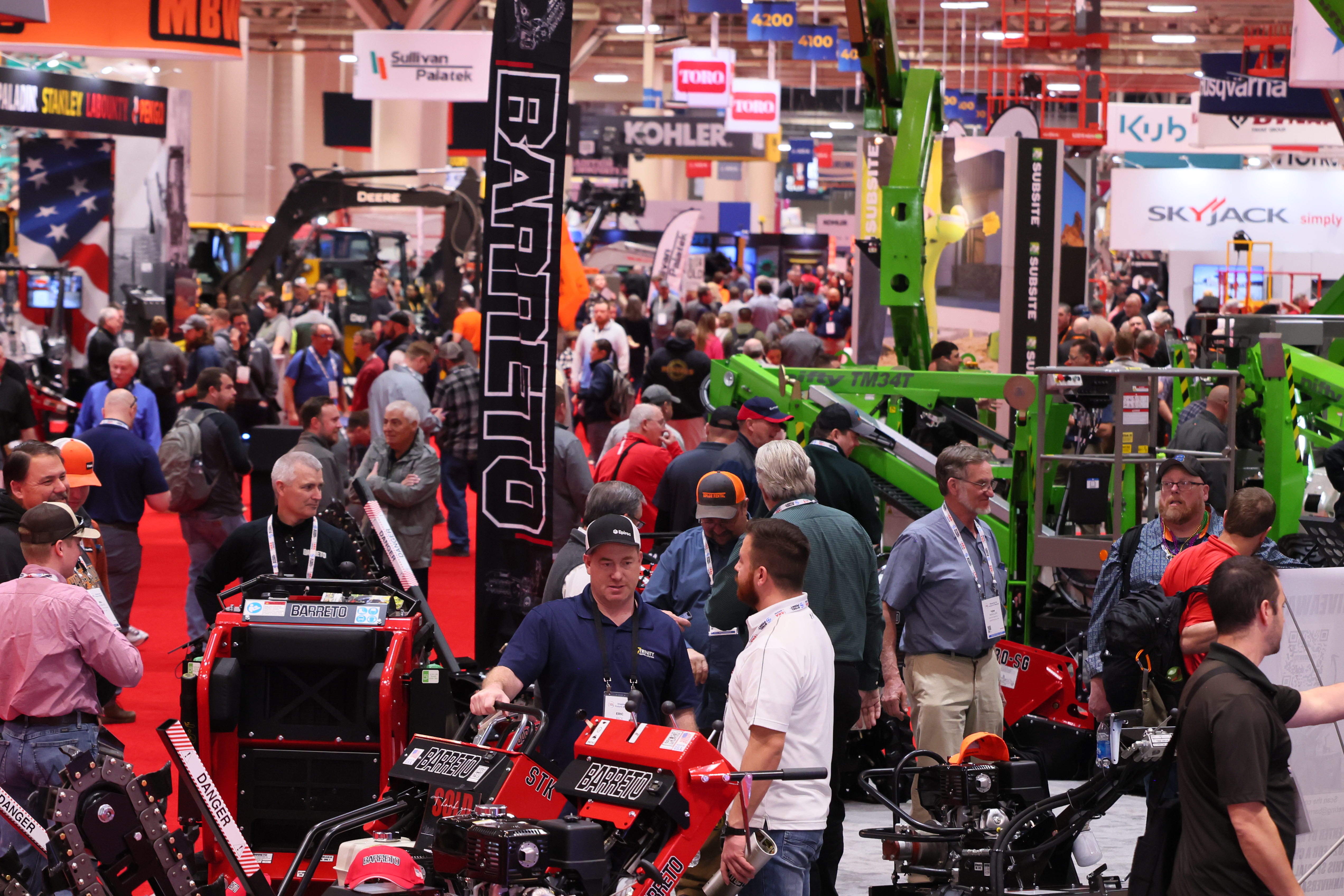 Crowded industrial machinery trade show with red and green equipment displays