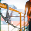 Construction safety equipment: carabiner hook on yellow railing with worker in background