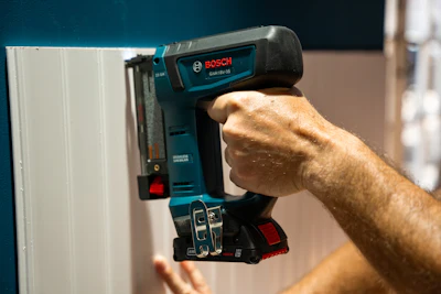 Bosch cordless nail gun being used to attach material near a white surface
