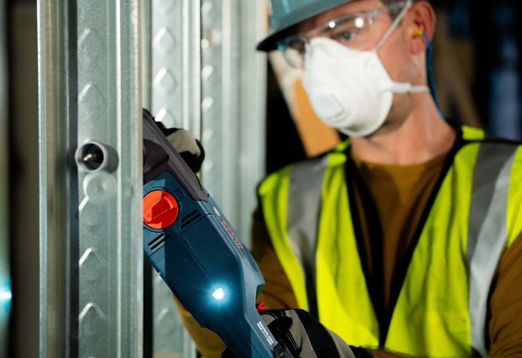 Construction worker wearing safety vest, hard hat, and mask using power tool
